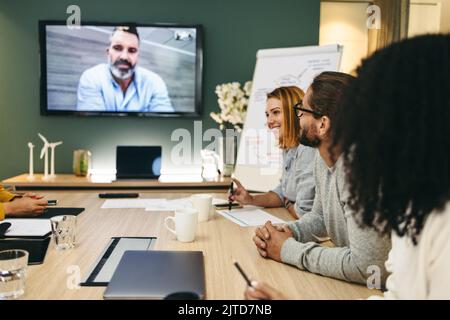 Moderne Geschäftsleute, die eine Videokonferenz in einem Sitzungssaal abhalten. Gruppe innovativer Geschäftsleute, die kreative Ideen austauschen, während sie an einem Stockfoto