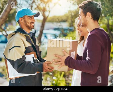 Hier, um Ihre erfolgreiche Lieferung zu übergeben. Ein Kurier, der eine Lieferung an ein junges Paar macht. Stockfoto