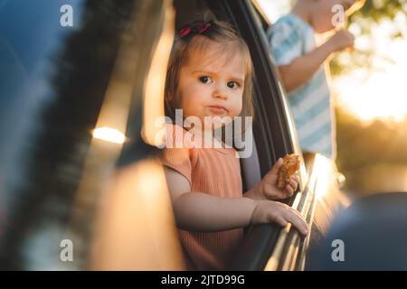 Zwei Kinder, die ihren Kopf aus den Fenstern eines Autos stecken und sich auf eine Autoreise oder Reise freuen. Roadtrip-Konzept. Sommerurlaub Spaß. Stockfoto