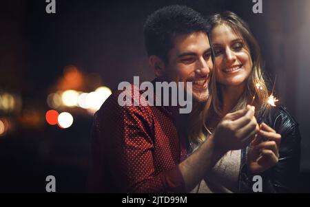 Zur Feier unserer Liebe ... ein glückliches junges Paar feiern mit Wunderkerzen draußen in der Nacht. Stockfoto