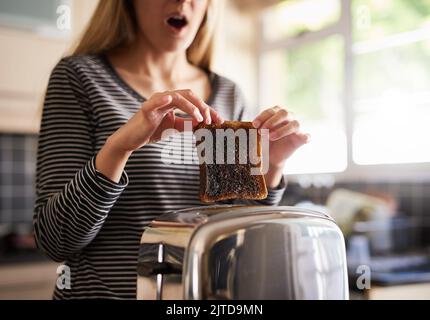 Ich ließ es zu lange zurück. Eine Frau, die zu Hause eine Scheibe verbranntem Toast aus einem Toaster entfernte. Stockfoto