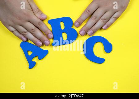 Kinderhände auf gelbem Hintergrund mit blauen Buchstaben. Das Konzept des Unterrichts von Kindern in der Schule Stockfoto