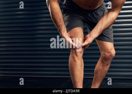 Den Schmerz in seinem Knie spüren. Studioaufnahme eines nicht erkennbaren, das sein Knie vor einem dunklen Hintergrund hält. Stockfoto