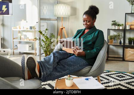 Porträt einer jungen schwarzen Geschäftsfrau, die im Büro ein digitales Tablet benutzt, während sie sich in der Lounge mit den Füßen nach oben entspannt Stockfoto