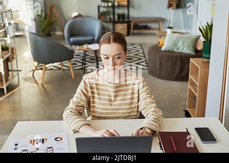 Hochwinkelporträt einer jungen kaukasischen Frau, die am Arbeitsplatz im Büro einen Laptop verwendet, Kopierbereich Stockfoto