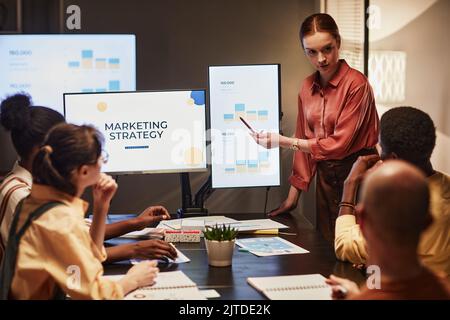 Porträt einer jungen Frau, die im schwach beleuchteten Büro eine Präsentation über Marketingtrends gibt Stockfoto