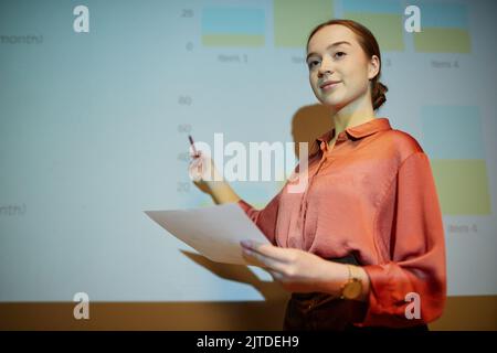 Porträt einer jungen Geschäftsfrau, die auf der Projektionsleinwand vorgeführt wird und Dokumente hält, Kopierfläche Stockfoto