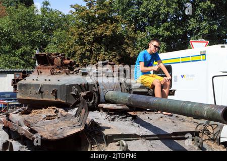 Odessa, Ukraine. 27. August 2022. Auf dem Turm sitzt ein junger Mann, der in den Farben der ukrainischen Flagge gekleidet ist. Einheiten des Operationskommandos "Süd" der Streitkräfte der Ukraine brachten russische militärische Ausrüstung, die in den Kämpfen für die Unabhängigkeit der Ukraine verbrannt war, zur Schau. Ausgestellt sind der Panzer T-90, zwei Transporter MT-LB, KAMAZ und ein gepanzerter Personentransporter. Kredit: SOPA Images Limited/Alamy Live Nachrichten Stockfoto