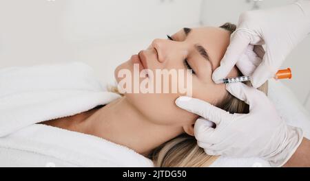 Schöne Frau während der Gesichtsmesotherapie zur Glättung von Mimik Falten um die Augen mit Kosmetikerin. Anti-Aging-Injektionen für Verjüngung und Lift Stockfoto