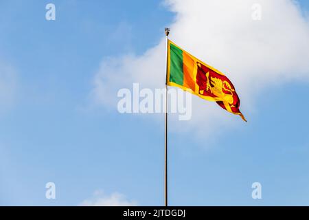 Die Flagge Sri Lankas oder die Sinha-Flagge steht an einem sonnigen Tag auf einem Fahnenmast unter bewölktem Himmel Stockfoto