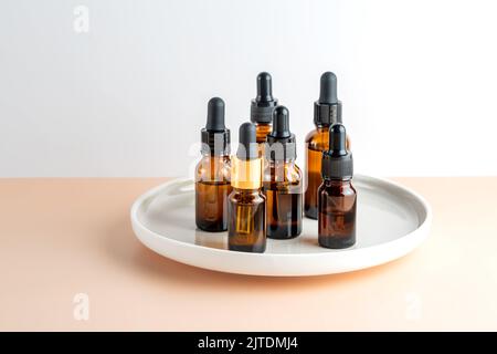 Kosmetikflaschen aus dunklem Glas tropfer mit Gesichtsserum oder ätherischem Öl auf einer Keramikschale. Kosmetikprodukte von Unbranded Beauty. Stockfoto