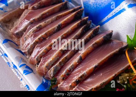 Nahaufnahmeangebot Katsuo-no-Tataki (leicht gebratene, in Scheiben geschnittene Bonito-Sashimi) im Lebensmittelbehälter des Supermarktes. Stockfoto