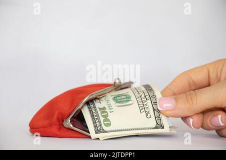 Hundert Dollar liegen in einer roten Brieftasche auf weißem Hintergrund, Finanzen und Wirtschaft, eine Frauenhand gibt Geld aus einer Brieftasche, Ausgaben Stockfoto