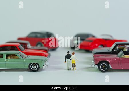 Ein Paar geht zwischen Oldtimern, Miniaturfiguren-Szene, Spielzeugautos, Stockfoto