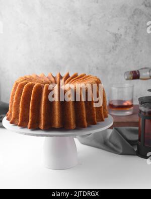 Rum-gebundener Kuchen auf einem weißen Kuchenständer, eingeweicht gebundener Kuchen, goldener Kuchen Stockfoto
