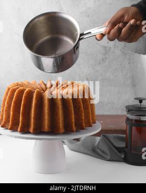Weibliche Hand gießt eine Rumsauce auf Rum-Bunt-Kuchen Stockfoto