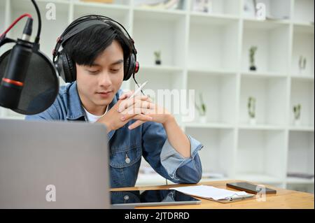 Professioneller asiatischer männlicher Podcaster oder Radiomoderator, der seine Podcast-Show im Studio konzentriert. Männlicher Influencer oder Podcaster-Konzept Stockfoto