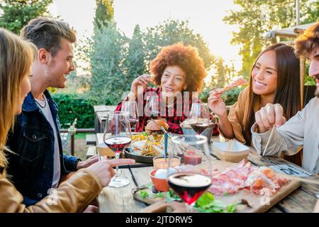 Eine Gruppe multiethnischer Freunde, die einen gesunden Lebensstil leben und lächeln und scherzen, während sie einen Aperitif machen und Rotwein im Pub-Restaurant im Freien trinken Stockfoto