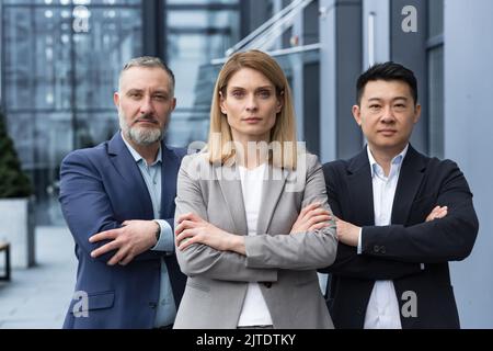 Ein erfolgreiches und seriöses Team aus drei Geschäftsleuten, Männer und Frauen, die sich mit gekreuzten Armen auf die Kamera konzentrierten, ein Porträt von Mitarbeitern außerhalb des Bürogebäudes Stockfoto
