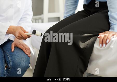 Neurologe untersucht eine junge Frau und überprüft ihren Knieruckreflex mit einem Hammer Stockfoto