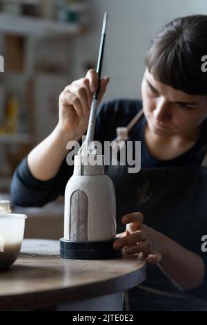 Glücklich konzentriert junge Handwerker malt Tonvase sitzen am Arbeitstisch Nahaufnahme Stockfoto