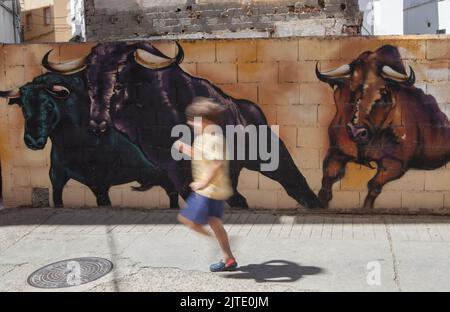 Losar, Spanien - 23.. August 2022: Kleiner Junge, der neben einer mit Graffiti verzierten Wand in Losar de la Vera, Caceres, Extremadura, Spanien, läuft Stockfoto