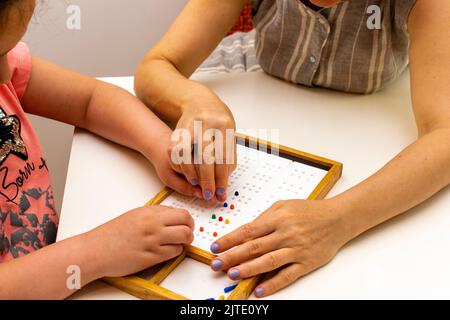 Die Hände eines Mädchens und die Hände eines Lehrers in Nahaufnahme. Braille-Tafel zum Erlernen des Alphabets Stockfoto