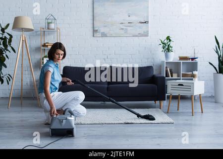 Brunette Frau Wechsel Staubsauger in der Nähe Teppich im Wohnzimmer Stockfoto