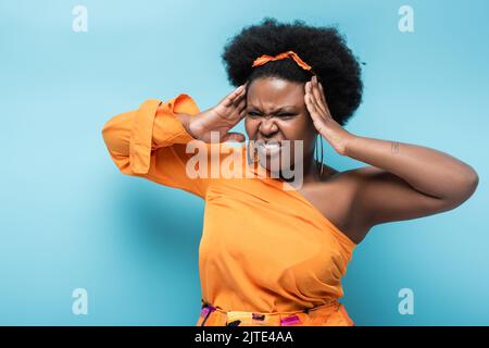 Lockige afroamerikanische Körper positive Frau in Reifen Ohrringe Kopfschmerzen auf blau, Stock Bild Stockfoto