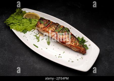 Gegrillte kopflose Makrele mit Kräutern auf einem Teller, auf grauem Beton Stockfoto