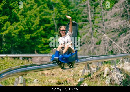 Mädchen reitet eine Achterbahn und Wellen. Bergumgebung mit Bäumen im Hintergrund Stockfoto