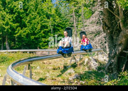 Skigebiet Bergbahn. Zwei Mädchen, eines hinter dem anderen, gehen die Skipiste hinunter. Wald und Bäume im Hintergrund Stockfoto