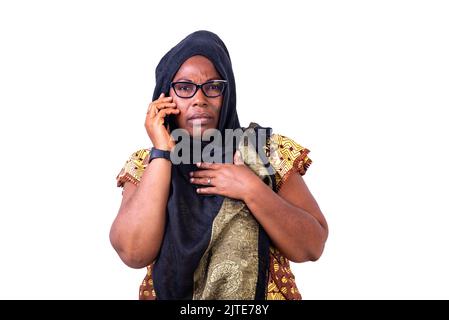 Seriöse muslimische reife Frau mit Brille, die auf dem Handy spricht. Stockfoto