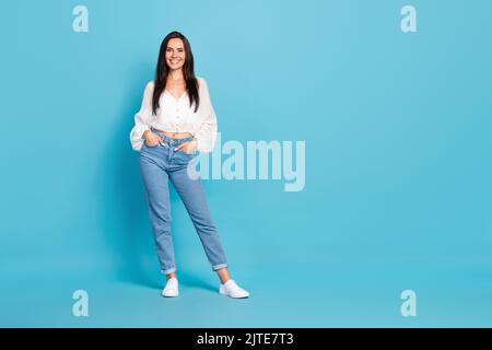 In voller Größe Foto von atemberaubenden zufrieden Mädchen legte Hände Taschen posiert leeren Raum auf blauem Hintergrund isoliert Stockfoto