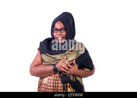 Die reife muslimische Frau trägt eine Brille und einen Schleier und leidet unter einem Herzinfarkt, während sie die Brust hält. Stockfoto