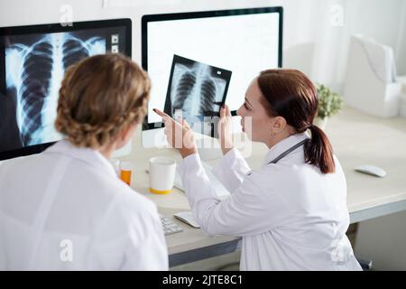 Junge weibliche Pneumologen diskutieren Röntgenaufnahmen von Patienten, die vom Coronavirus geborgen wurden Stockfoto