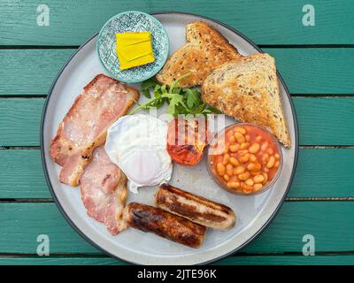 Gebratenes Frühstück mit pochiertem Ei, Speck, gebackenen Bohnen, Wurst und geröstetem Brot Stockfoto