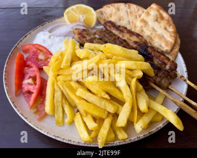 Griechische Souvlaki-Spieße mit Pommes Frites, Tomaten, Tsatziki-Sauce und Pita-Brot Stockfoto