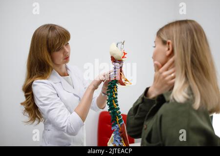 Orthopäde oder Neurologe zeigt den weiblichen Patienten die Problembereiche am Modell der Wirbelsäule und erklärt die Ursache ihrer Schmerzen Stockfoto