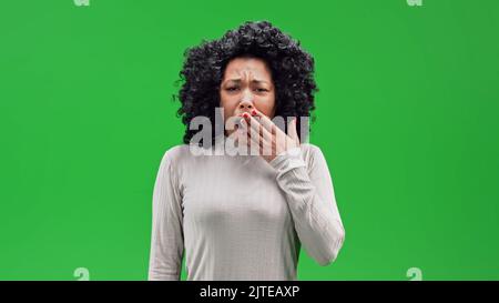 Eine afrikanische Frau mit lockigen Haaren stehend und gähnend im Chroma-Key-Hintergrund Stockfoto