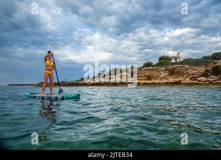 Frau, die auf einem Surfbrett unter einem dramatischen Himmel paddelt, Estalella, Küste von Llucmajor, Mallorca, Balearen, Spanien Stockfoto