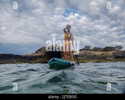 Frau, die auf einem Surfbrett unter einem dramatischen Himmel paddelt, Estalella, Küste von Llucmajor, Mallorca, Balearen, Spanien Stockfoto