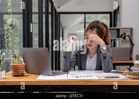 Gestresste Geschäftsfrau, die von zu Hause aus auf einem Laptop arbeitet, sieht besorgt, müde und überwältigt aus. Stockfoto