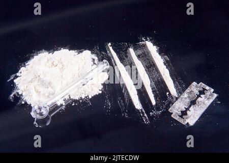 Stapel weißer Puderdrogen und Rauchrohr aus Glas. Rasiermesser- und Kokainlinien zum Schnauben. Stockfoto