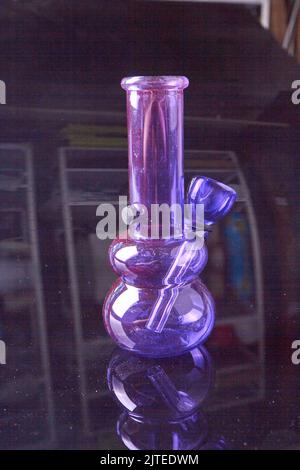 Vertikale Nahaufnahme einer violetten Glasbong auf einer Glasoberfläche. Unkrauchgerät. Stockfoto