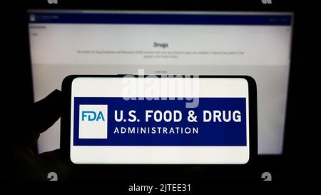 Person, die das Smartphone mit dem Logo der US-amerikanischen Food and Drug Administration (FDA) auf dem Bildschirm vor der Website hält. Konzentrieren Sie sich auf die Telefonanzeige. Stockfoto