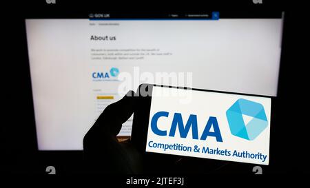 Person, die das Smartphone mit dem Logo der British Competition and Markets Authority (CMA) auf dem Bildschirm vor der Website hält. Konzentrieren Sie sich auf die Telefonanzeige. Stockfoto