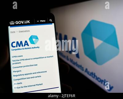 Person mit Mobiltelefon und Website der British Competition and Markets Authority (CMA) auf dem Bildschirm mit Logo. Konzentrieren Sie sich auf die Mitte des Telefondisplays. Stockfoto