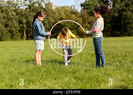 Glückliche Kinder springen durch den Hula Hoop Reifen im Park Stockfoto