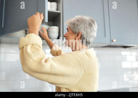 Glückliche Frau, die zu Hause das Schließfach in der Küche öffnet Stockfoto